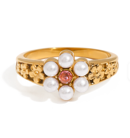 Gold ring with pearl and pink gemstone center on a white background